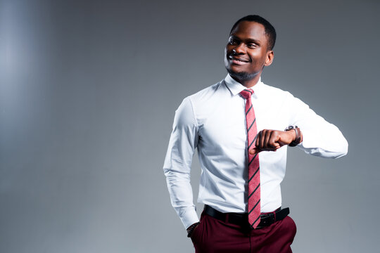 Handsome african american businessman in shirt holds up his hand with clock and looks to the side
