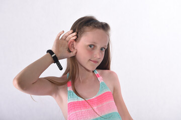 A beautiful school-age girl in the studio on a white background stands forward and holds her ear...