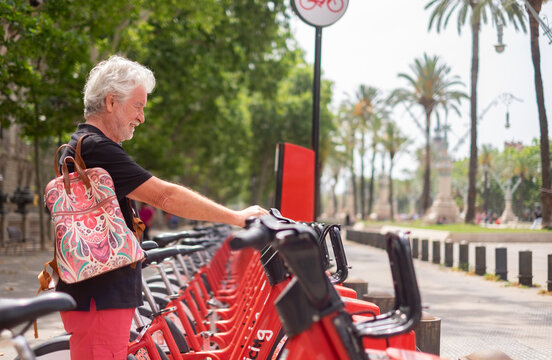 Senior man smile renting an electric bicycle in public park. Bearded caucasian people enjoying freedom and healthy lifestyle
