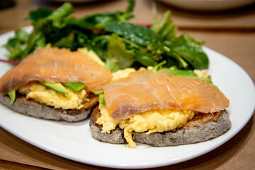 Scrambled eggs with fresh avocado and salmon served on two toasts  wheat bread with fresh lettuce on white plate for a healthy breakfast