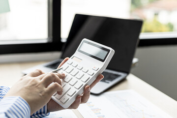 Female auditor pressing white calculator, she is a private company auditor, she is reviewing numbers of company financial statements before presenting them to senior management. Audit concept.