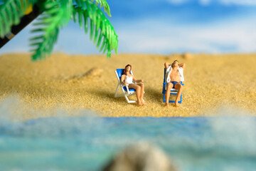 Miniature people toy figure photography. Men and girl couple relaxing on beach chair when daylight at seaside.