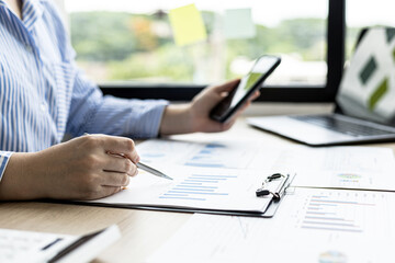 A businesswoman checking sales briefs and sending text messages to her via mobile phone, she is reviewing data and analyzing sales data to plan to manage more sales growth. Sales management concept.