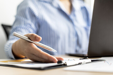 A businesswoman is reviewing the sales summary sheet from the sales department, she is reviewing the data and analyzing the sales data to plan to manage more sales growth. Sales management concept.