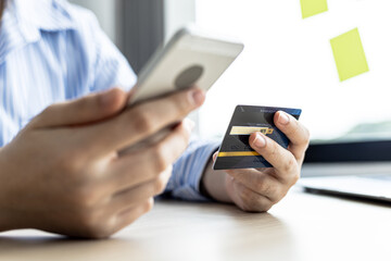 A woman holding a cell phone and credit card, she fills in her credit card information in a mobile shopping app to pay for the purchase. Online shopping concept using credit card payments.
