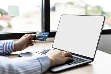 Woman typing on a laptop keyboard and holding a credit card, she fills in her credit card information on a laptop shopping app to pay for the order. Online shopping concept using credit card payments.