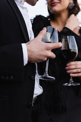 cropped view of elegant couple holding glasses of red wine