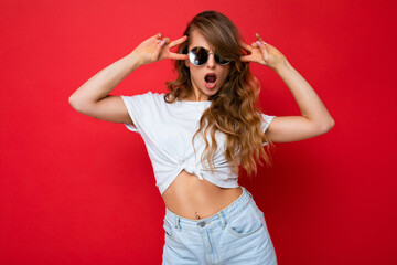Attractive positive funny young blonde woman wearing everyday stylish clothes and modern sunglasses isolated on colorful background wall looking at camera and having fun