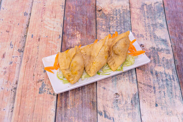 tray of fried samosas stuffed with lamb meat on a bed of iceberg lettuce and grated carrots on a wooden table
