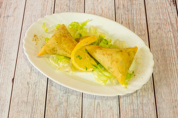 Portion of vegetable samosa served in a Hindu restaurant with iceberg lettuce and a slice of lemon with pepper and ground curry