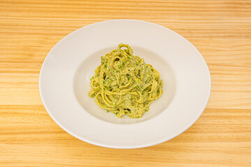 Italian tagliatelle pasta recipe with pesto and pistachio sauce on white plate and yellow wooden table