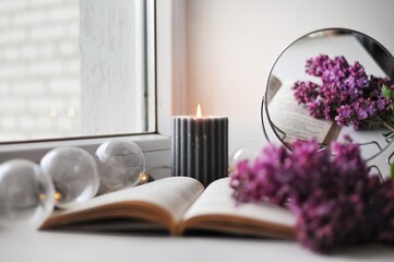 Romantic cozy corner at home with opened book, candle and with a lilac bush.