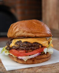 Classic cheeseburger with beef burger, pickle, cheese, tomato, onion, lettuce and ketchup mustard on blurred background.