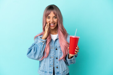 Young mixed race woman drinking a fresh drink isolated on blue background shouting with mouth wide open
