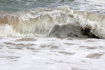 Nature details: Front on view of an ocean wave breaking near the shore on shallow white foamy water