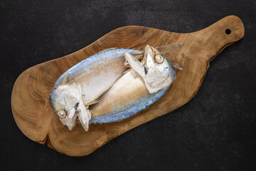 top view shot of steamed mackerel in olive natural wood cutting board on the dark tone texture background