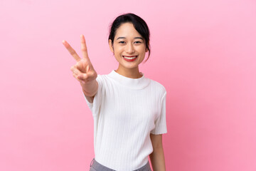 Young Vietnamese woman isolated on pink background smiling and showing victory sign