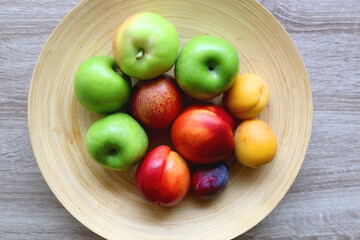 Wooden bowl with various colorful fruit on dark background. Top view.