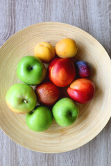 Wooden bowl with various colorful fruit on dark background. Top view.