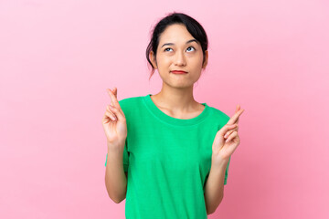 Young Vietnamese woman isolated on pink background with fingers crossing and wishing the best