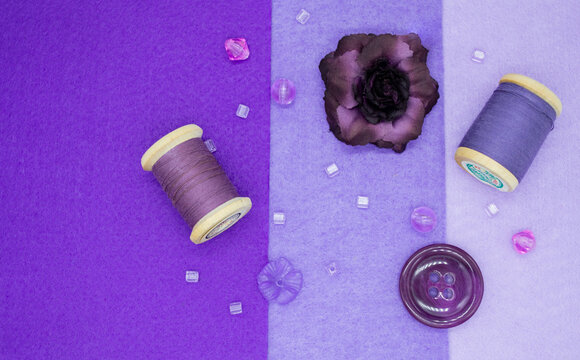 Purple sewing items: felt in three shades of lilac, wooden spools with thread, beads, buttons, and a purple rose
