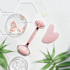 Pink Quarts stone face roller and serum capsules in round glass dish and hexagon glass. Gua sha...