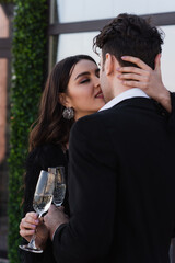 man and woman clinking glasses of champagne and kissing outside