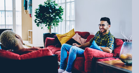 Joyful Middle Eastern man in spectacles laughing at joke of best female friend enjoying free time, funny hipster guys satisfied with good conversation during weekend meeting in loft home interior