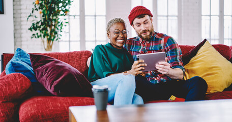 Millennial diverse marriage enjoying weekend leisure for networking websites via application on touch pad, smiling couple in love reading positive news while browsing internet via digital tablet