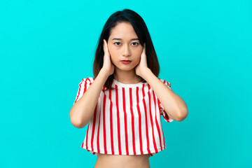 Young Vietnamese woman isolated on blue background frustrated and covering ears