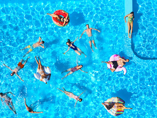Aerial of friends having party in swimming pool with inflatable flamingo, swan, mattress. Happy...