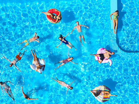 Aerial of friends having party in swimming pool with inflatable flamingo, swan, mattress. Happy young people relax at luxury resort on sunny day. View from above. Girls in bikini sunbathing in a sun.