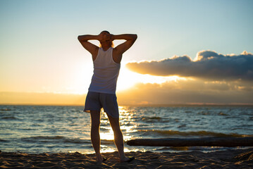 Fototapeta premium A humorous portrait of a brutal man in a T-shirt and boxers on the beach at sunset
