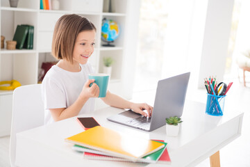 Photo portrait little girl watching online lesson with laptop drinking tea typing answer