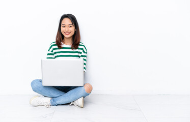 Young Vietnamese woman with a laptop sitting on the floor isolated on white wall keeping the arms...
