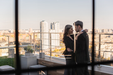 side view of couple hugging on terrace behind blurred window of restaurant