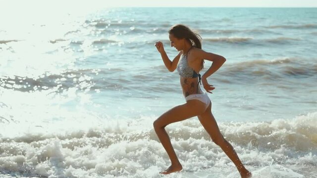 slow motion footage of happy joyful fitness girl in bikini running along sea beach with waves