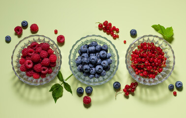 Set of different berries in glass bowls on green background with shadows. healthy eating, detox and vitamin concept. top view