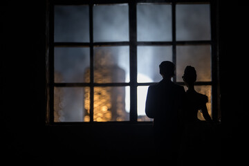 A realistic dollhouse living room with furniture and window at night. Romantic couple sitting on window. Artwork table decoration with handmade realistic dollhouse. Selective focus.