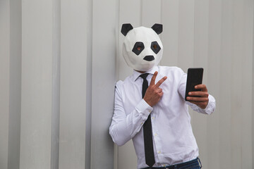 Man in white shirt, tie and panda mask taking smartphone selfie against wall