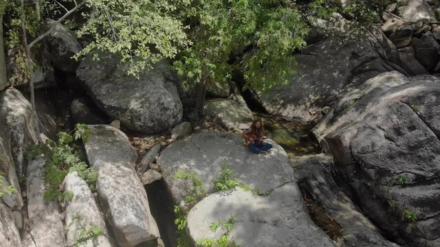 Man with dreadlocks sitted on a rock playing guitare - drone shot