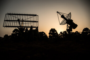 Space radar antenna on sunset. Silhouettes of satellite dishes or radio antennas against night sky....