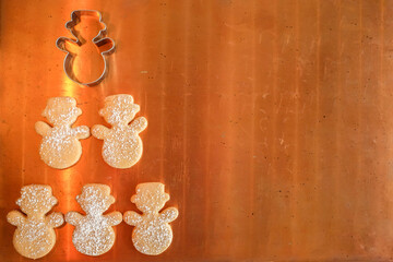 Minimalist Christmas background with copy space: overhead of homemade snowman cookies covered with icing sugar and a cookie cutter on copper  background