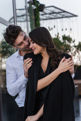 elegant man hugging cheerful woman in black blazer