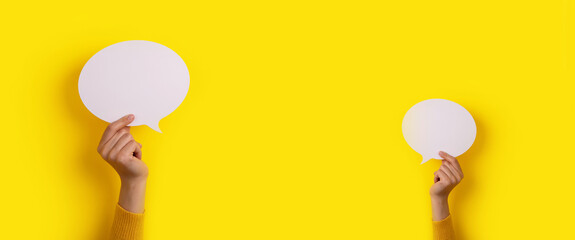 hands holding dialogue icon over yellow background, panoramic mock-up image
