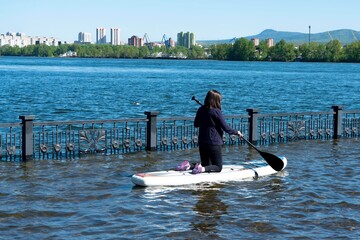 A girl rides a SUP board with a paddle on the river. Russia, Krasnoyarsk - June 2021.