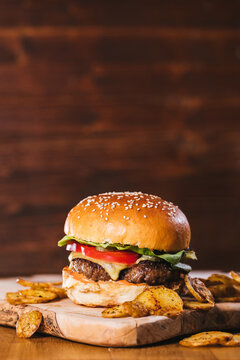 Classic cheeseburger with potato wedges served on a rustic  wooden board