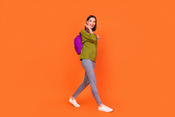 Fototapeta na wymiar Full body profile photo of lovely brunette millennial lady go look empty space wear bag shirt jeans isolated on orange color background