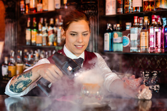 Professional bartender with flavor blaster preparing cocktail in bar