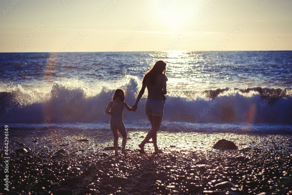 Wall mural Mother with child girl at the sea beach on sunset